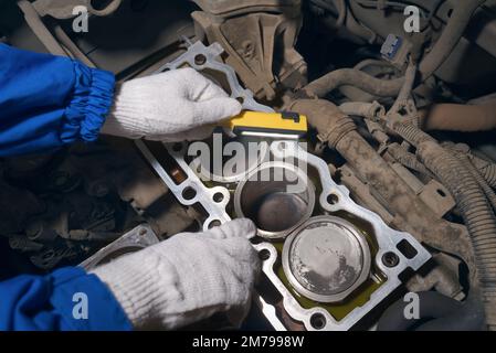 Ein Automechaniker überprüft einen Automotor mit einer Taschenlampe. Zylinderblock mit Kolben ohne Deckel. Reparaturdienstleistungen. Wartung, Reparatur und Diagnose Stockfoto