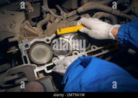 Ein Automechaniker inspiziert einen Automotor mit einer Taschenlampe. Zylinderblock mit Kolben ohne Deckel. Reparaturdienstleistungen. Wartung, Reparatur und diagnose Stockfoto