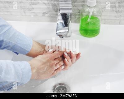 Handwäsche mit Seife oder Gel unter fließendem Wasser im Waschbecken, Sauberkeit und Hygiene, Frauenhände in blauem Hemd Stockfoto