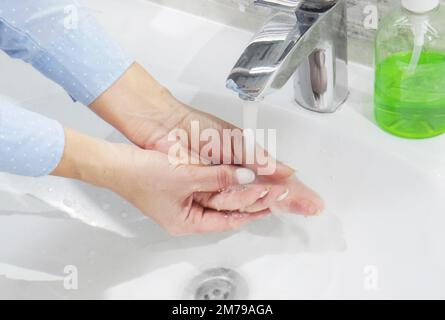 Handwäsche mit Seife oder Gel unter fließendem Wasser im Waschbecken, Sauberkeit und Hygiene, Frauenhände in blauem Hemd Stockfoto