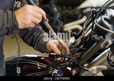 Ein Elektriker lötet elektrische Drähte an elektrische Geräte in einem Motorrad. Nahaufnahme. Transportkonzept Stockfoto