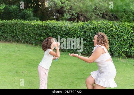 Mutter und Tochter spielen mit Blasen in einem Park. Stockfoto