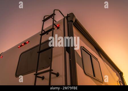 Nahaufnahme eines hinteren Teils des modernen Wohnmobils mit Stufen zum Dach im Licht der untergehenden Sonne. Motto „Motorheim Reisen“. Stockfoto