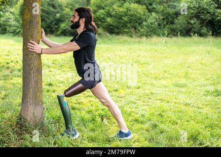 Ein behinderter Sportler mit amputiertem Bein beginnt mit dem Stretching, bevor er im Park im Freien läuft Stockfoto