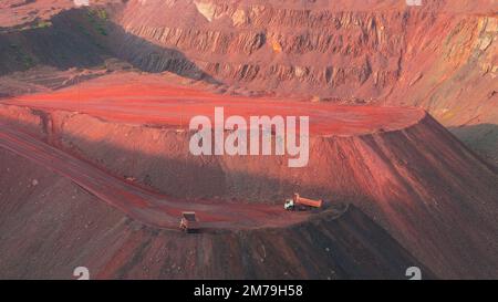 Bulldozer und Lastwagen in Steinbrüchen mit rotem Boden. Eisenerzbergbau in Kriviy Rih, Ukraine. Industrielandschaft Stockfoto