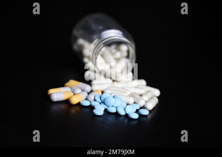 Pillen auf einem schwarzen Holztisch, Variation der Medikamente in Kapseln, die aus einer Flasche verstreut sind. Hintergrund für Pharmazie, Antibiotika, Vitamine Stockfoto