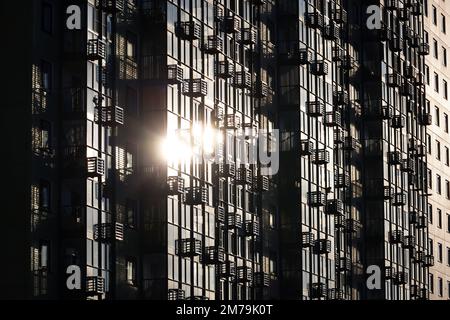 Silhouette eines neuen Wohngebäudes, Sonne spiegelt sich in den verglasten Balkonen mit Körben für die Klimaanlage wider. Hausbau Stockfoto