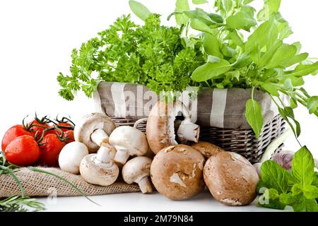 Frische weiße Pilze auf weißem Hintergrund in einem Korb mit Kräutern und Tomaten Stockfoto