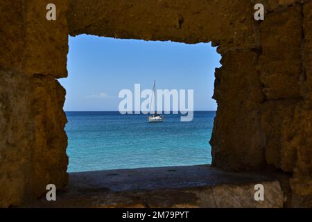 Rhodos, Griechenland - Mai 2022: Segelboot auf dem Meer in der Nähe des Hafens mit Blick durch ein Loch in der Altstadt. Stockfoto