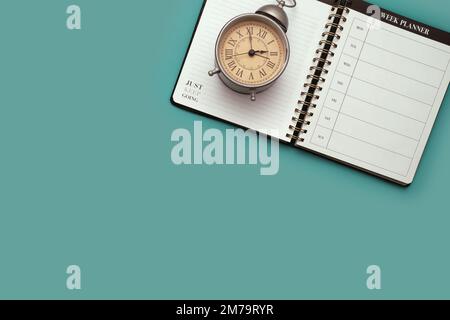 Über dem Kopf liegend ein Kalender-Planer-Notizbuch und ein Vintage-Wecker vor blauem Hintergrund Stockfoto