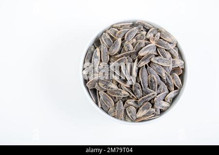 Sonnenblumenkerne in weißer Schüssel auf weißem Hintergrund. Gesalzene Sonnenblumenkerne in der Schüssel. Stockfoto