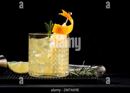 Penicillin-alkoholischer Cocktail mit Scotch, Whiskey, Honig-Ingwersirup, Zitronensaft und Eis in Glas mit Orangenschale garniert. Schwarzer Hintergrund Stockfoto