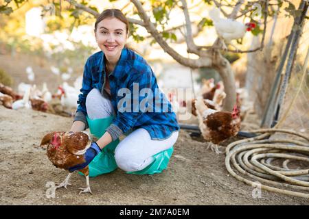 Lächelnde Landwirtin, die in der Hühnerfarm für die Hühnerzucht sorgt Stockfoto