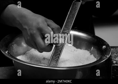 Koch reißt Parmesankäse mit feiner Reibe in Nahaufnahme Stockfoto