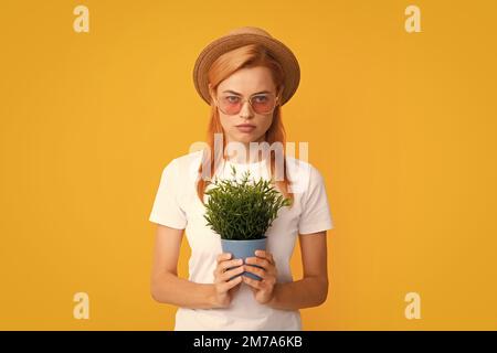 Fröhliche junge Frau mit Topfpflanze. Isolierter gelber Hintergrund, Nahaufnahme im Hochformat. Pflanzenpflege und Hausgartenarbeit. Frau pflanzt Blumen in den Topf. Stockfoto