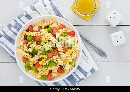 Frischer, hausgemachter, farbenfroher veganer Nudelsalat mit Bohnen, Mais, Tomaten, Gurke und grünem Paprika, serviert in der Schüssel Stockfoto