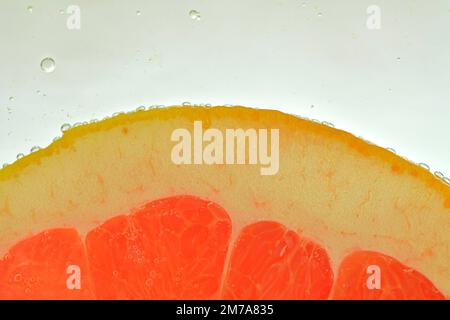 Nahaufnahme der roten Grapefruitscheibe im Wasserhintergrund. Konsistenz des kühlenden Fruchtgetränks mit Makroblasen an der Glaswand. Flaches Design.