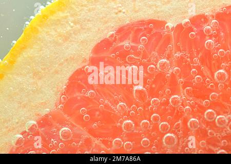 Nahaufnahme einer frischen Grapefruitscheibe auf weißem Hintergrund. Eine Scheibe rote Grapefruit in sprudelndem Wasser auf weißem Hintergrund, Nahaufnahme. Horizontales Bild. Stockfoto