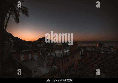 Ein Weitwinkelaufnahme des Sonnenuntergangs von einem Dach in einem Haus in einer brasilianischen Favela in Rio mit Blick auf das beruhigende Meer und die Dächer der Umgebung Stockfoto