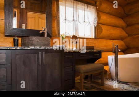 Waschbecken aus Holzkohleholz mit Waschbecken aus zerquetschten Flusssteinen, die mit Epoxid und weißer freistehender ovaler Badewanne im Badezimmer verklebt sind. Stockfoto