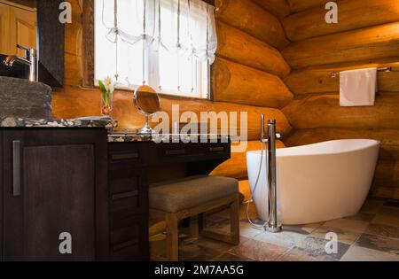 Waschbecken aus Holzkohleholz mit Waschbecken aus zerquetschten Flusssteinen, die mit Epoxid und weißer freistehender ovaler Badewanne im Badezimmer verklebt sind. Stockfoto