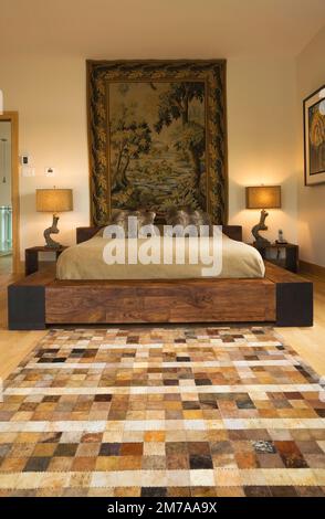 Kingsize-Bett mit Holzrahmen und malerischen Wandteppichen im Hauptschlafzimmer im Obergeschoss im modernen kubistischen Stil. Stockfoto