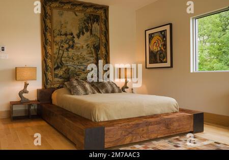 Kingsize-Bett mit Holzrahmen und malerischen Wandteppichen im Hauptschlafzimmer im Obergeschoss im modernen kubistischen Stil. Stockfoto