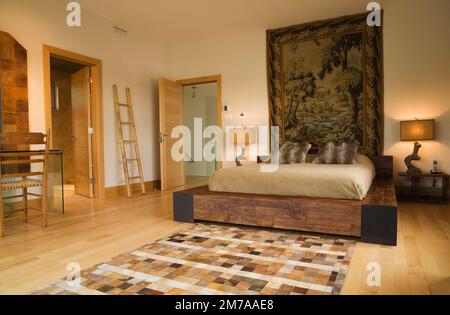 Kingsize-Bett mit Holzrahmen und malerischen Wandteppichen im Hauptschlafzimmer im Obergeschoss im modernen kubistischen Stil. Stockfoto