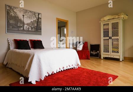 Queen-Size-Bett und weißer Holzschrank mit Gitterrahmen im Gästezimmer im oberen Stockwerk im modernen kubistischen Stil Haus. Stockfoto