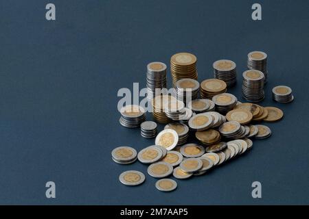 Mexikanische Peso-Münzen, stapelbar und auf einer blauen Oberfläche verstreut, mit Kopierraum. Stockfoto