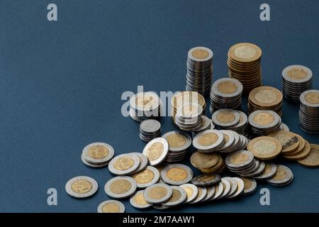 Mexikanische Peso-Münzen, stapelbar und auf einer blauen Oberfläche verstreut, mit Kopierraum. Stockfoto