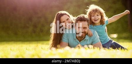 Banner der glücklichen Familie, die auf Gras liegt. Junge Mutter und Vater mit Kind Sohn spielen im Park zusammen auf dem grünen Gras ruhen. Freundliche Familie Stockfoto