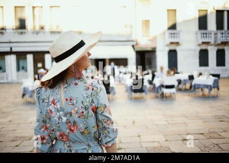 Von hinten gesehen, eine moderne Reisende Frau in Blumenkleidung mit Hut, um Venedig, Italien, zu besichtigen. Stockfoto