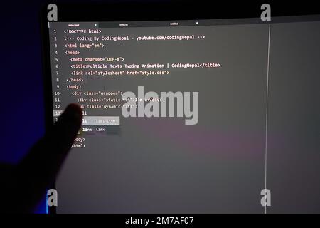 Schreiben des Computercodes, der auf dem Monitor angezeigt wird und mit dem Finger auf eine Codezeile zeigt Stockfoto