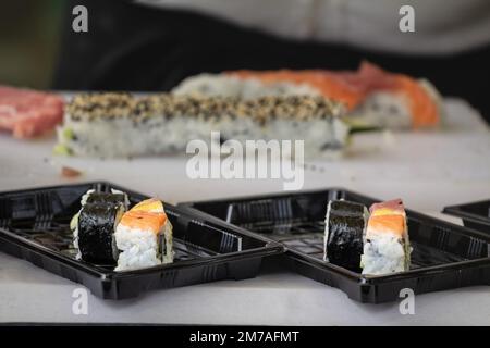 Bild von sushis, wie sie sich vorbereitet und in schwarze Plastikboxen verpackt, um geliefert zu werden. Stockfoto