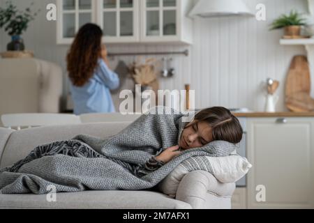 Unglückliches erschöpftes Teenager Mädchen bedeckt mit einer Decke, die auf dem Sofa neben der Küche lag und an Grippe litt Stockfoto