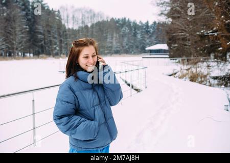 Schöne Frau, die ruhig wartet, am Telefon spricht, in einer verschneiten Landschaft Stockfoto