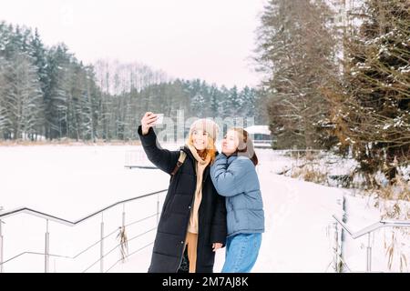 Zwei Frauen, die im Winter mit einem Telefon befreundet sind, machen im Winter ein Selfie Stockfoto