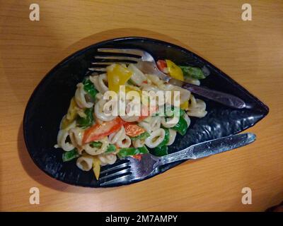 Tintenfisch-Pasta, serviert in einer entworfenen schwarzen Schüssel mit Löffeln Stockfoto