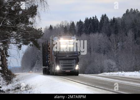 Neuer, schwarzer Volvo FH16 Holztransporter des Transports Å Björkqvist transportiert Holzlasten auf der Straße, Fernlicht kurz eingeschaltet. Salo, Finnland. 27. Dezember 2021. Stockfoto