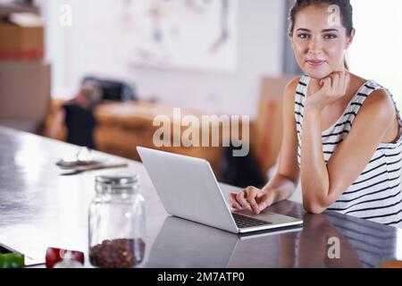 Heute Abend wird das Essen fantastisch. Porträt einer attraktiven jungen Frau, die ihren Laptop in der Küche benutzt. Stockfoto
