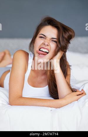 Nichts geht über ein bisschen Morgendummheit. Eine junge Frau, die im Bett liegt und Gesichter zieht. Stockfoto