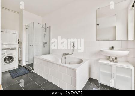 Ein weißes Badezimmer mit schwarzem Fliesenboden und eine Waschmaschine in der Ecke neben der Badewanne ist an der Wand Stockfoto