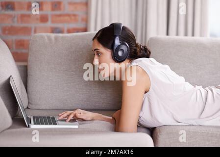 In Kontakt bleiben im digitalen Zeitalter. Eine junge Frau auf einem Sofa, Kopfhörer und einen Laptop. Stockfoto