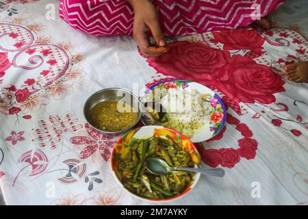 Ein authentischer Blick von oben auf ein traditionelles bangladeschisches Hausgericht mit verschiedenen Currysorten und kleinen Fischen Stockfoto