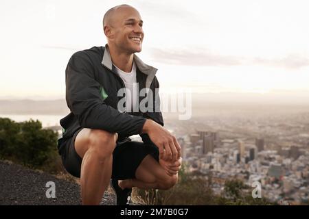 Genießen Sie die Aussicht nach seinem morgendlichen Lauf. Ein junger Mann in Sportbekleidung, der den Sonnenaufgang sieht. Stockfoto