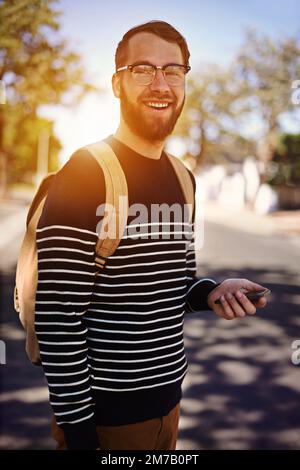 Ich Stelle sicher, dass ich verbunden bin, wenn ich unterwegs bin. Porträt eines trendigen jungen Mannes, der sein Handy draußen hält. Stockfoto