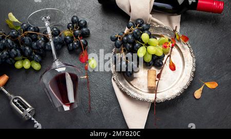 Ein Foto von Gläsern Rotwein mit einer Flasche, Trauben und einem alten Korkenzieher und Korken, aufgenommen von oben auf dunklem Hintergrund. Draufsicht. Pano Stockfoto