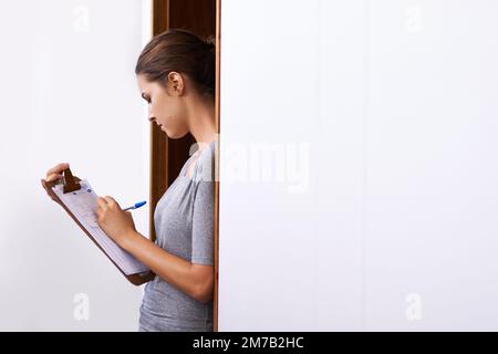 Zufriedenheit mit Unterschrift unterschrieben. Eine attraktive junge Frau, die auf ihr Klemmbrett schreibt. Stockfoto