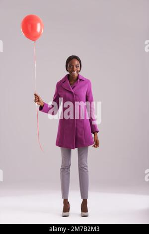 Es sind die einfachen Dinge, die mich zum Lächeln bringen. Studiofoto einer jungen Frau mit einem einzigen roten Ballon. Stockfoto